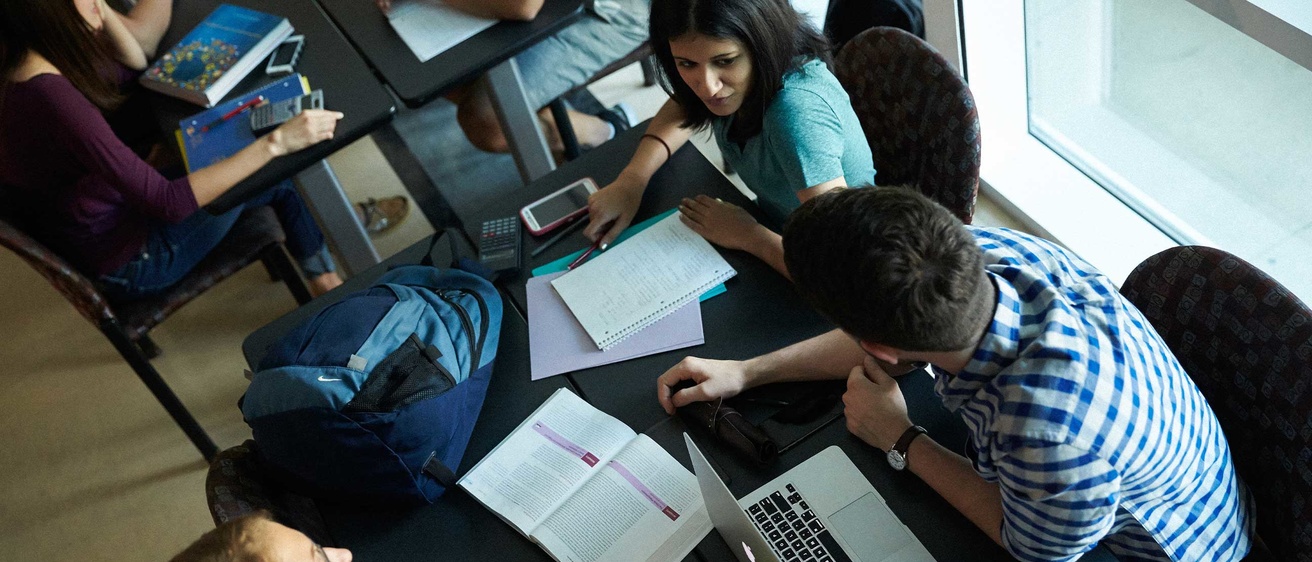 Students sitting at table with laptops and notebooks